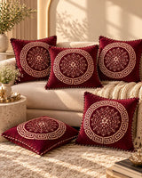 Burgundy cushion covers featuring intricate gold floral medallions, Greek-key borders and decorative piping on a cream sofa.