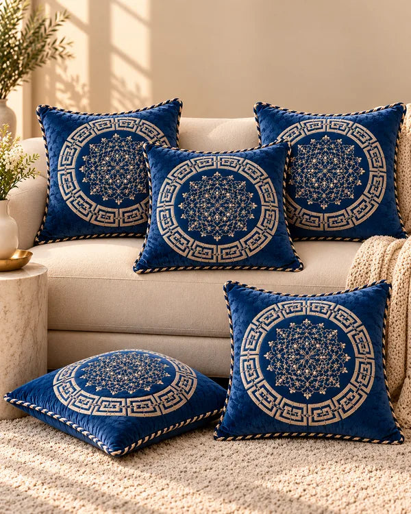 Navy blue decorative cushion covers with intricate gold circular medallions and Greek-key geometric borders arranged on a cream sofa.